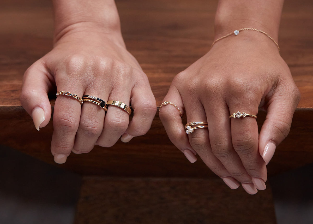 Two hands wearing multiple rings on a wooden surface with a blurred background