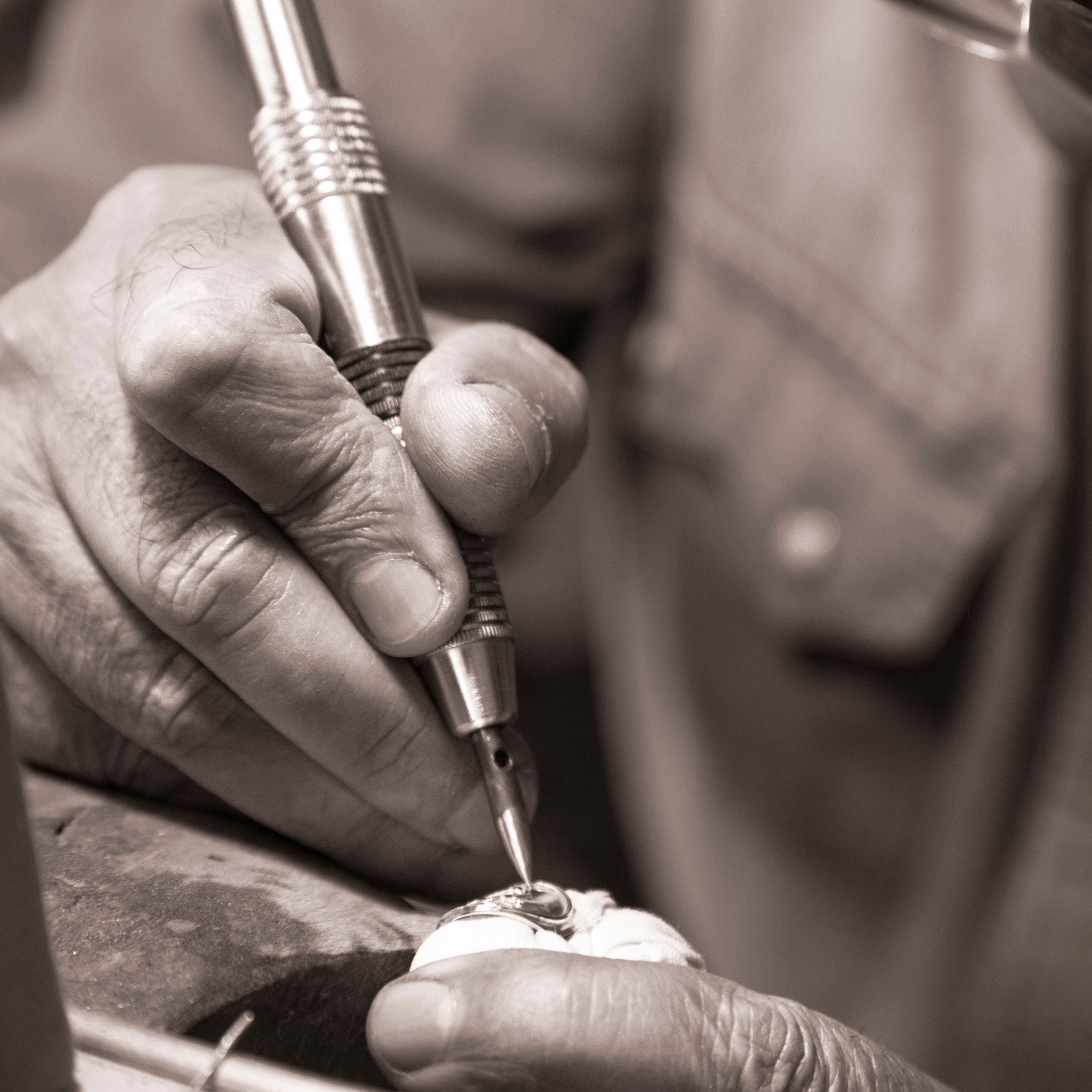 Close-up of a person's hands working on a small object with a tool, likely in a jewelry-making context.